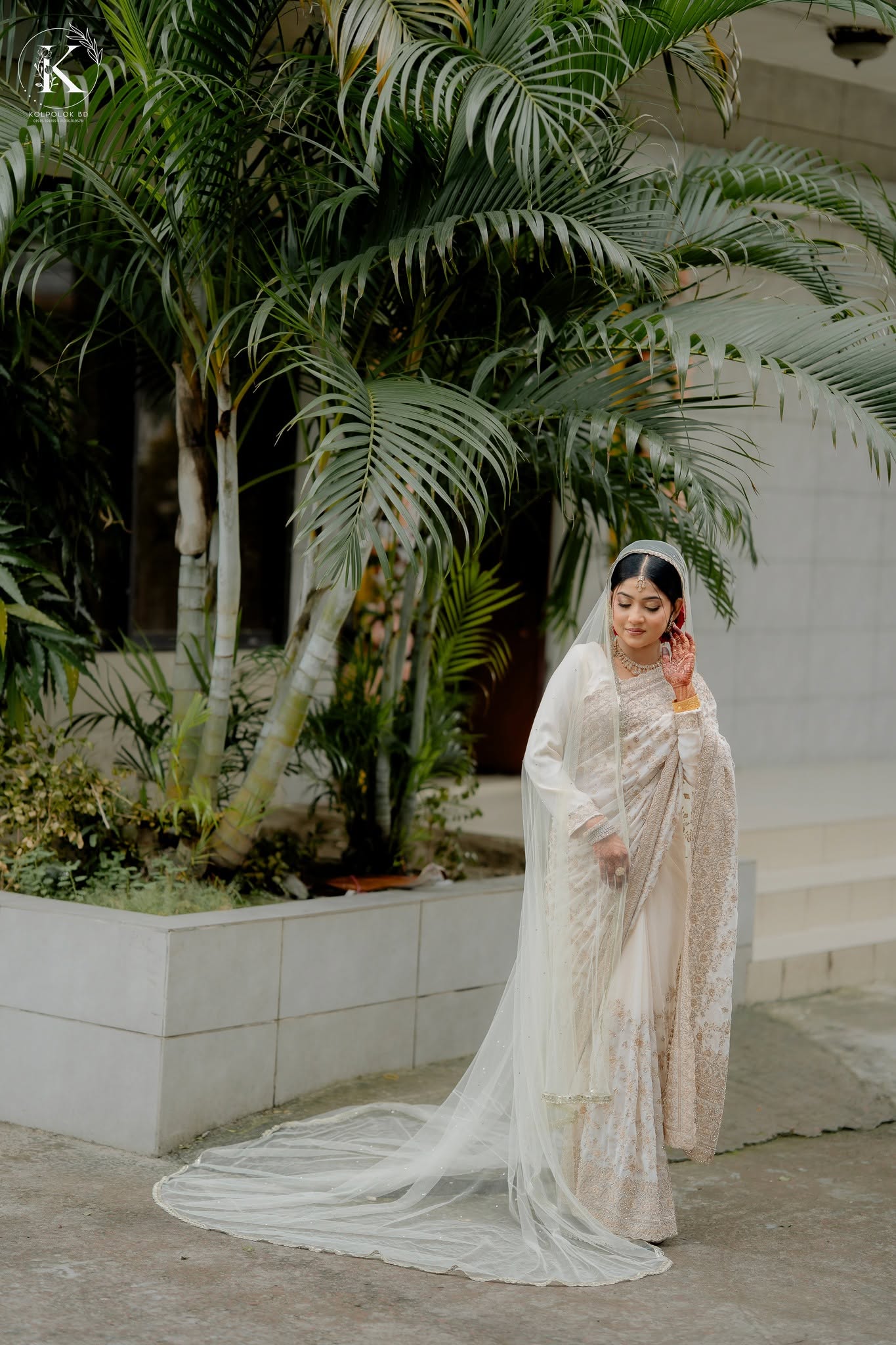 Bride in white standing beneath palm leaves